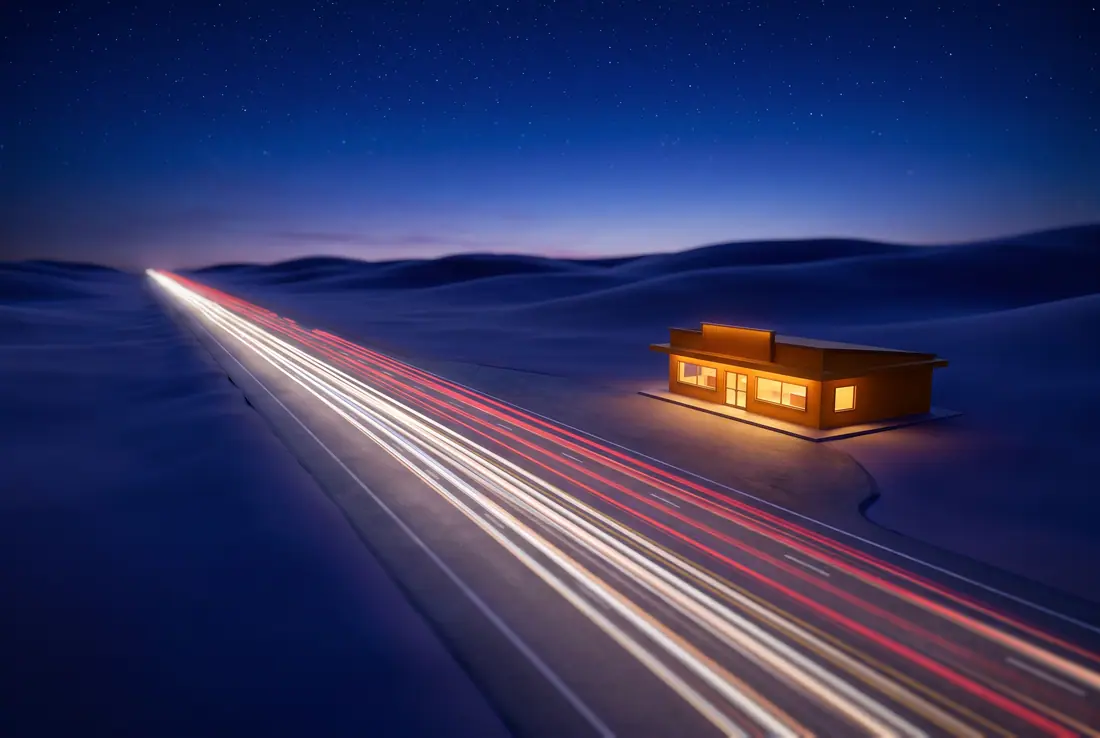 Light trails on a prairie highway at night beside one glowing roadside building