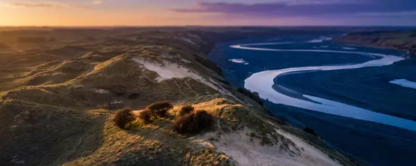 Grass-covered sand hills above a winding river valley in the last light of the day